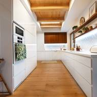 Kuchyně je vyrobená z bílých lesklých MDF desek, doplňuje je ořechové dřevo